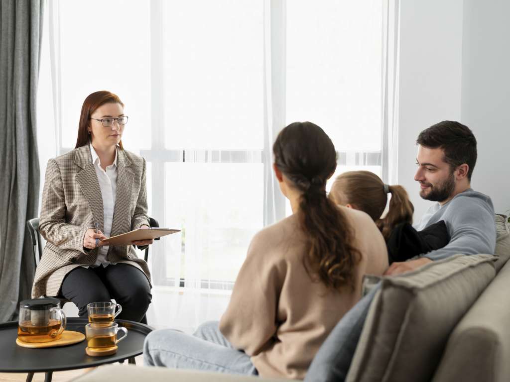 Latino father and young child holding a teddy bear speak with a family mediator in a bright, welcoming child-friendly contact centre.